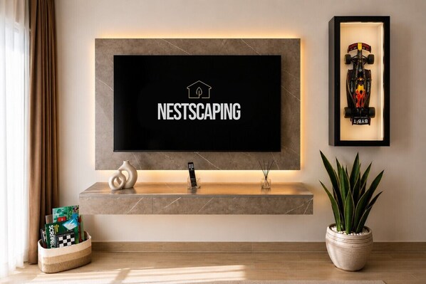 En moderne stue med et monteret tv, der viser 'NESTSCAPING', et stilrent konsolbord med en vase, en fjernbetjening og et indrammet billede af en racerbil.