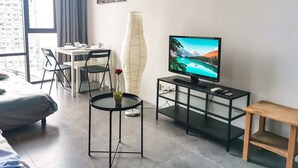 Ein modernes Wohnzimmer mit Fernseher, Essbereich und großem Fenster mit Vorhängen.