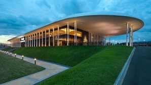 A modern, curved building with a glass facade and a flat roof, surrounded by a well-maintained lawn and a paved walkway. - Lovely Studio Trefoil Near Setia City Mall & Sccc (Shah Alam)