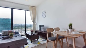A modern living room with a sofa, coffee table, and dining area with chairs and a table. - Lovely Studio Trefoil Near Setia City Mall & Sccc (Shah Alam)