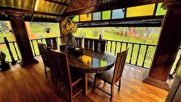 A round table with chairs, a vase of flowers, and a view of a garden through a balcony with a black railing.