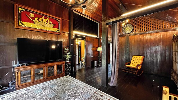 A wooden interior with a television, a patterned rug, a decorative wall piece, and a chair.