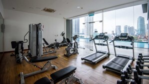 Ein Fitnessstudio mit unterschiedlichen Trainingsgeräten, großen Fenstern mit Stadtblick und einem Holzboden.