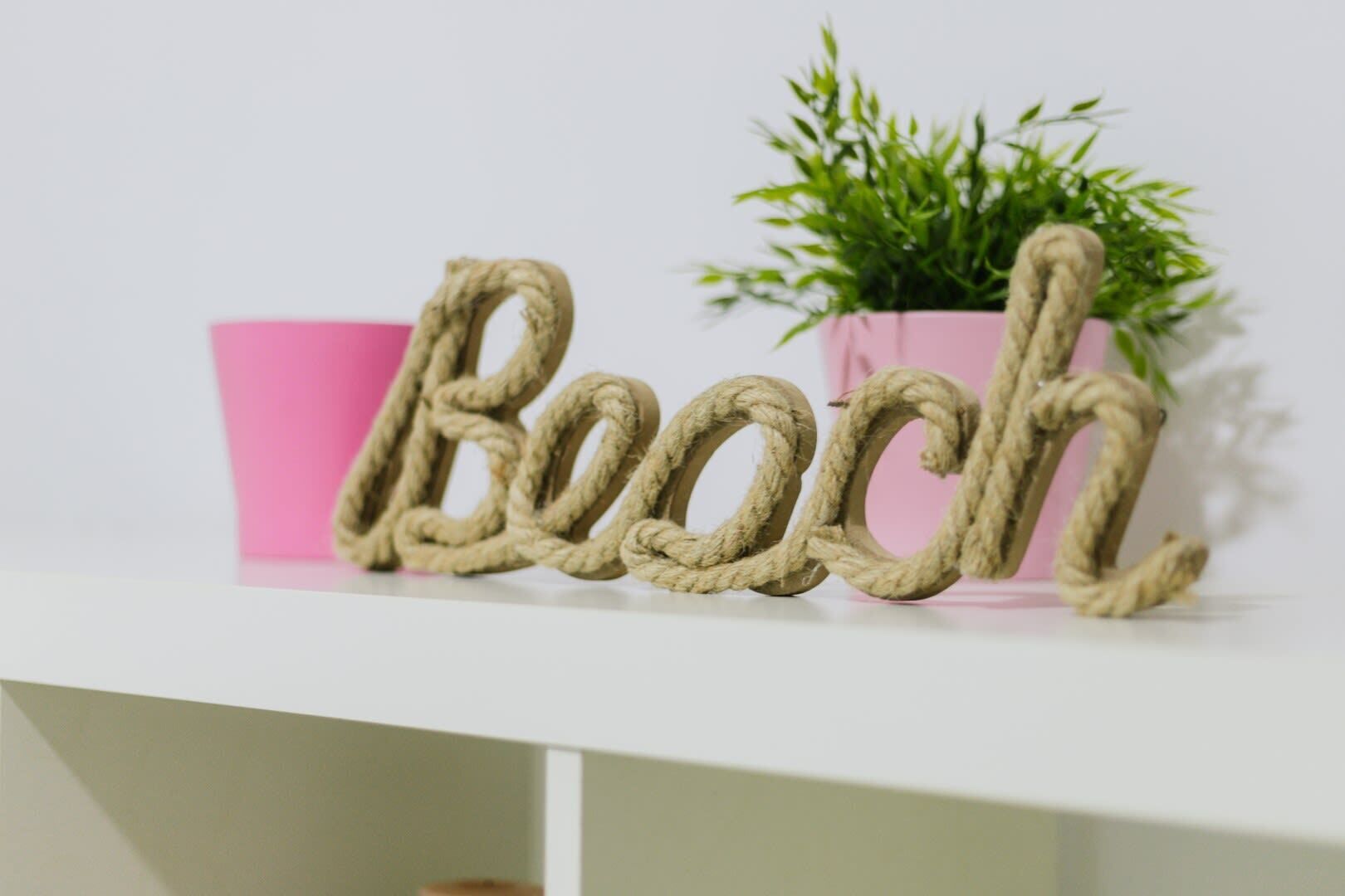 A shelf with a rope decoration spelling "Beach" and a small potted plant.