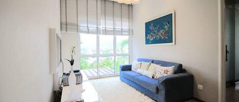 A modern living room with a blue sofa, a white rug, and a painting on the wall.