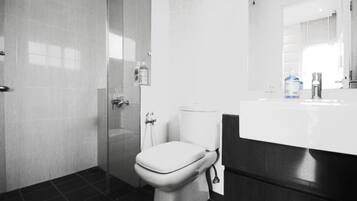 A bathroom with a toilet, a glass shower enclosure, and a white sink with a mirror above it.