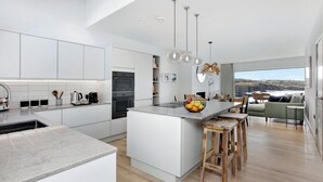 A modern kitchen with white cabinets, a central island, and a dining area with a view.