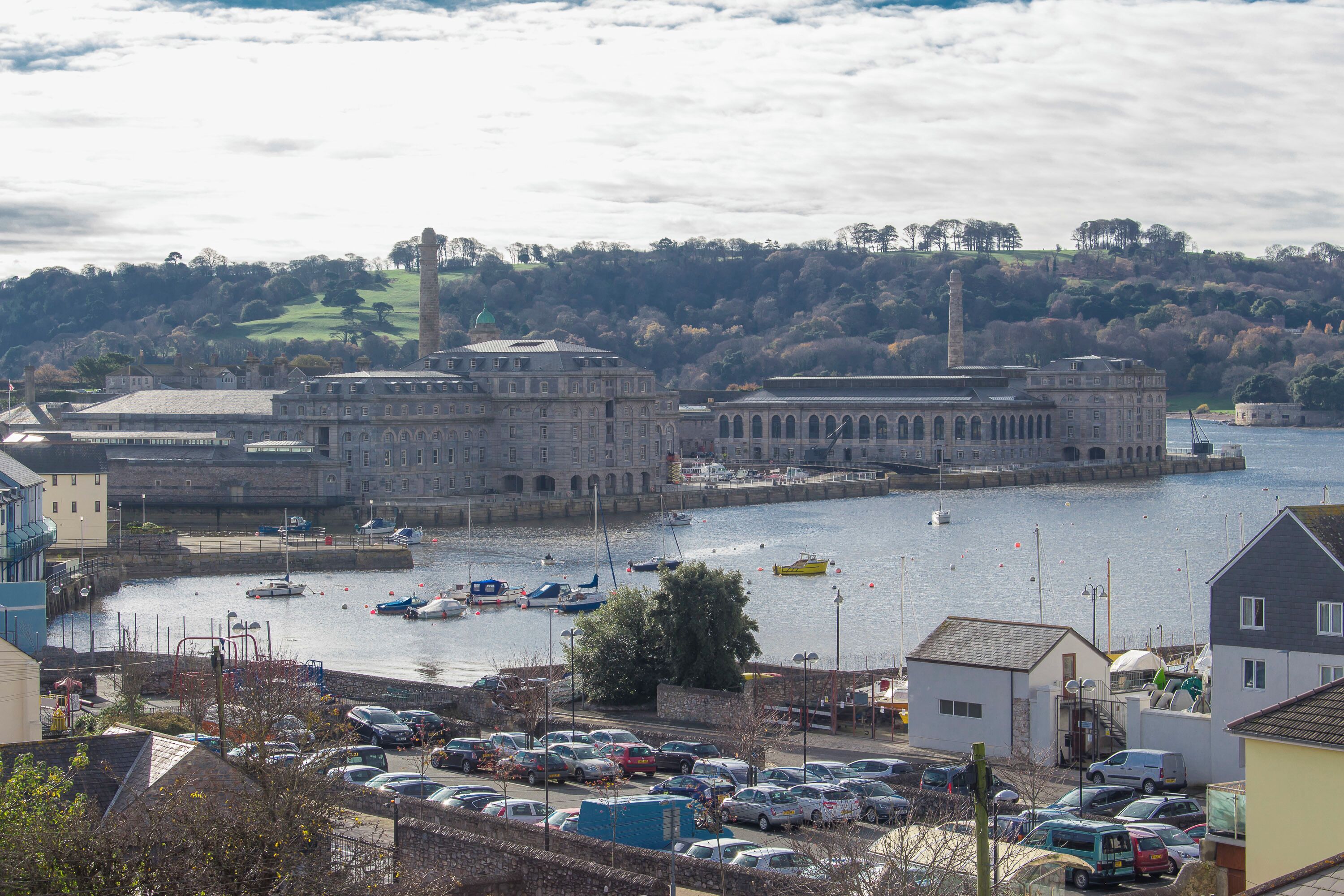 Un pueblo costero con un edificio histórico, un puerto deportivo con barcos y un área de estacionamiento.
