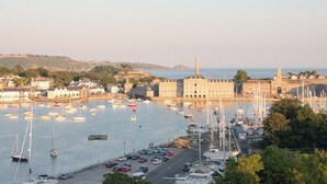 A harbor with boats, a large building, and a lighthouse in the background.