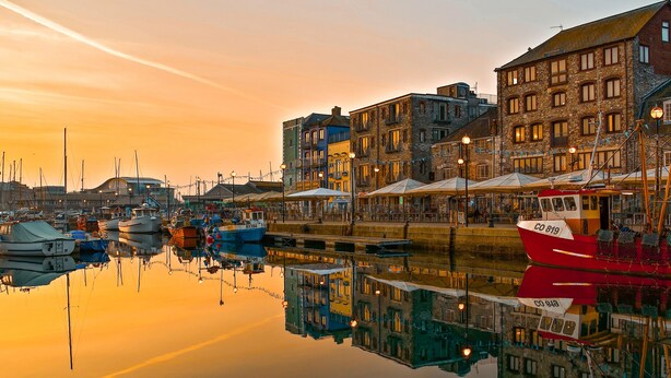 A harbor with boats docked, buildings with multiple stories, and a clear sky.