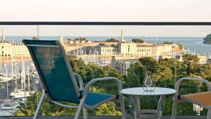 A balcony with two chairs and a small table, overlooking a marina with boats and buildings.