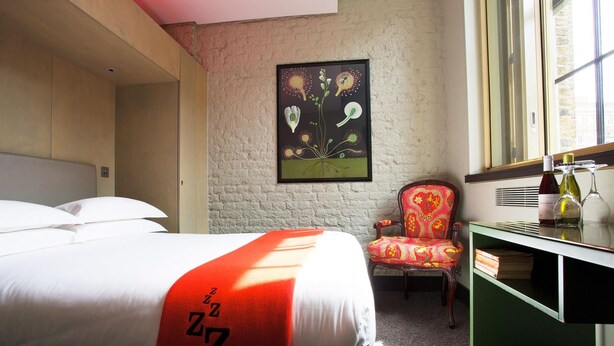 A hotel room with a bed, a chair, a desk with a mirror, and a window. - The Zetter (London)