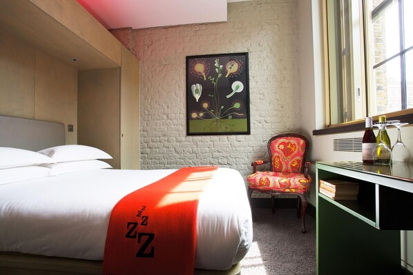 A hotel room with a bed, a chair, a desk with a mirror, and a window. - The Zetter (London)