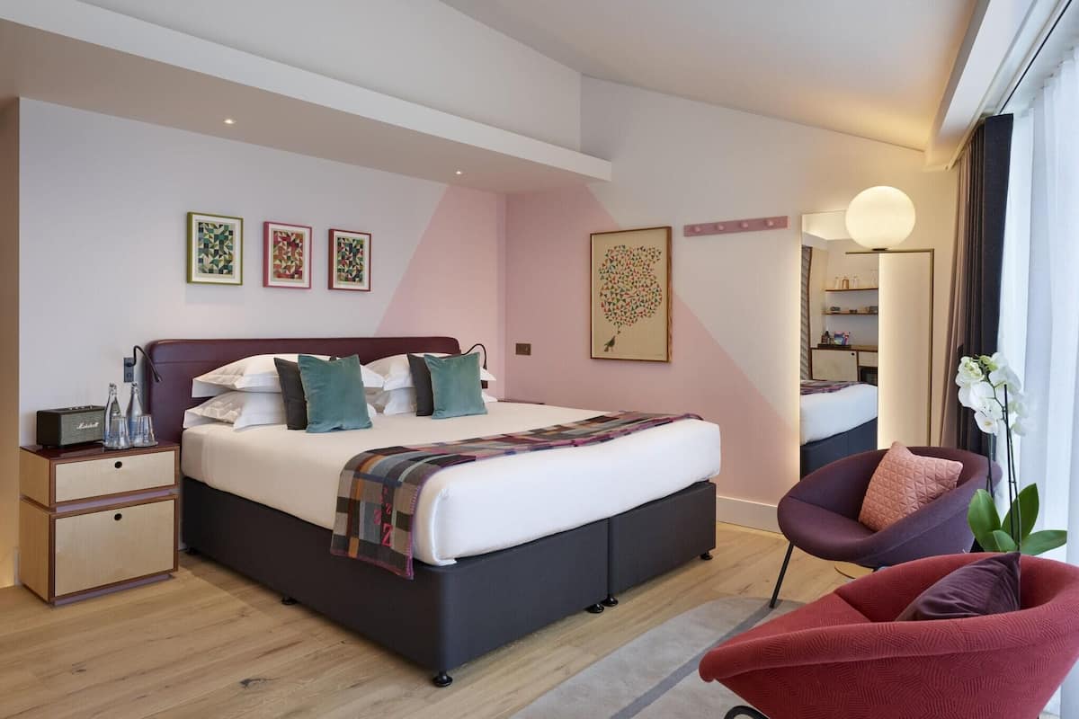 A modern bedroom with a large bed, bedside tables, a chair, and artwork on the walls.