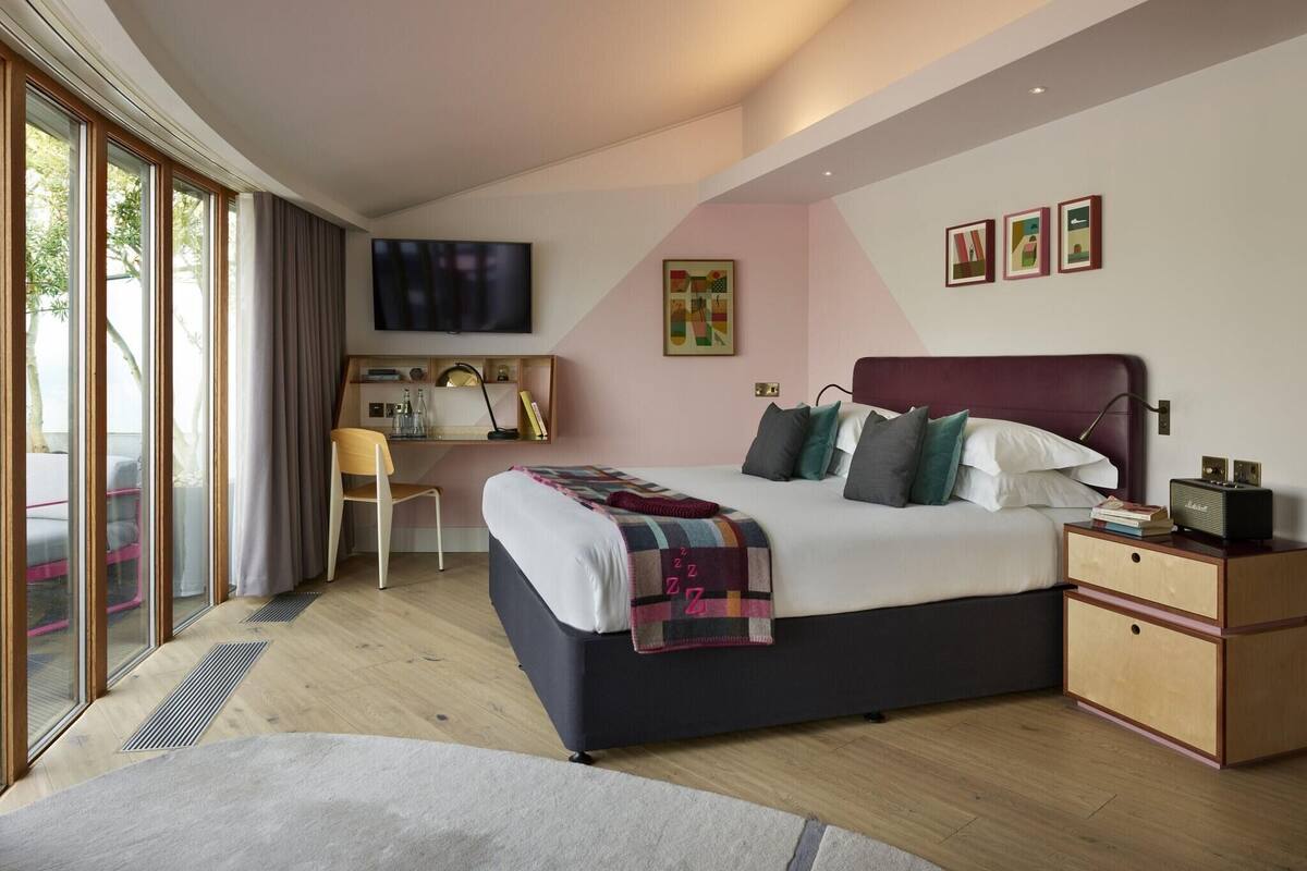 A modern bedroom with a large bed, a desk, and a TV.