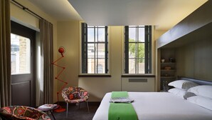 A hotel room with a bed, two chairs, a red floor lamp, and large windows. - The Zetter (London)
