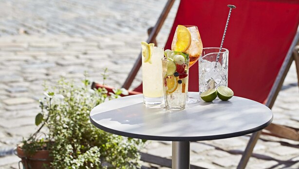 A table with three drinks, each with fruit garnishes, and a potted plant beside it. - The Zetter (London)