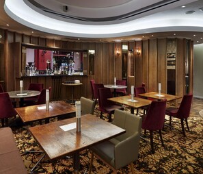 A restaurant with round tables and red chairs, a bar area, and a patterned carpet. - The Zetter (London)