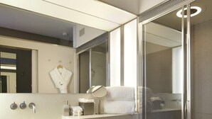 A modern bathroom with a large mirror, a toilet, a shower enclosure, and a vanity with a sink and towel rack. - The Zetter (London)