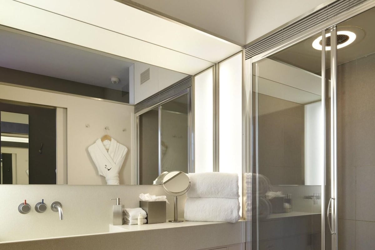 A modern bathroom with a large mirror, a toilet, a shower enclosure, and a vanity with a sink and towel rack.