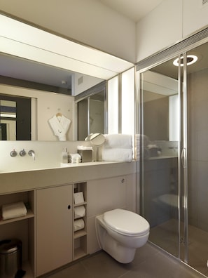 A modern bathroom with a large mirror, a toilet, a shower enclosure, and a vanity with a sink and towel rack. - The Zetter (London)
