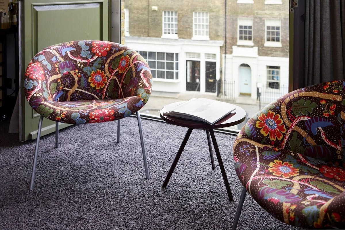 A room with two patterned armchairs, a small table, and a view of a building through an open door.