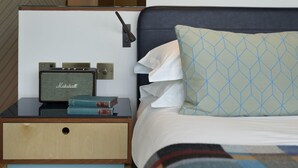 A neatly made bed with a patterned pillow, a bedside table with a vintage radio, and a wall-mounted light. - The Zetter (London)