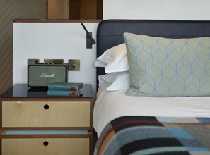 A neatly made bed with a patterned pillow, a bedside table with a vintage radio, and a wall-mounted light. - The Zetter (London)