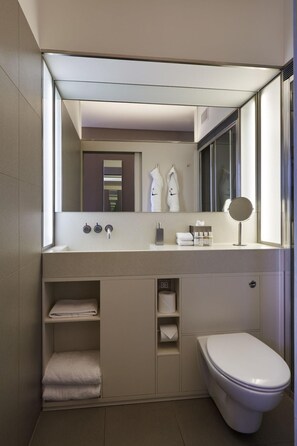 A modern bathroom with a large mirror, a toilet, and built-in shelves for towels. - The Zetter (London)