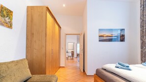 A bedroom with a bed, a wooden wardrobe, a sofa, and a hallway leading to a dining area. - Copper House - Old Town Constance (Konstanz)