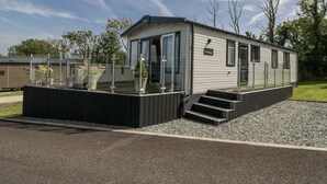 A modern mobile home with a glass-enclosed porch, a nameplate reading "Windermere," and a gravel driveway. - Winscales Rest (Workington)