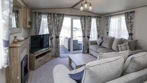 A living room with a flat-screen TV, sofa, coffee table, and curtains. - Winscales Rest (Workington)