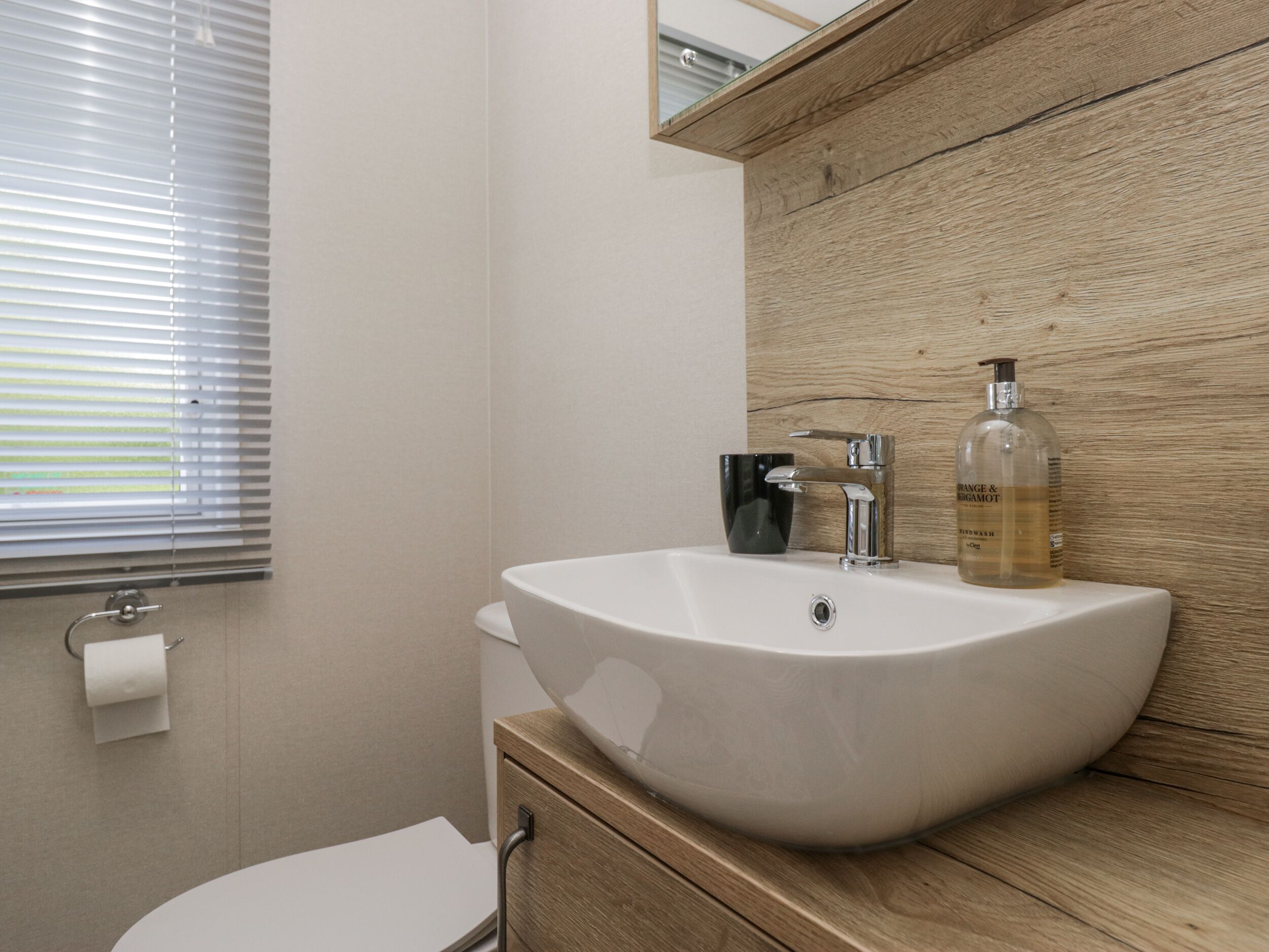 Een badkamer met een witte wastafel, een zwarte beker en een fles handzeep.