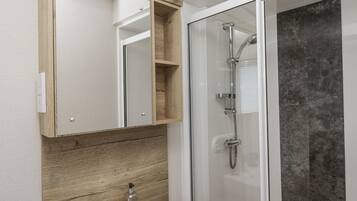 Un baño con tocador de madera, un espejo, un lavamanos y ducha con mampara de vidrio.