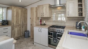 A modern kitchen with wooden cabinets, a stainless steel range hood, a built-in oven, and a sink with a blue basin. - Winscales Rest (Workington)