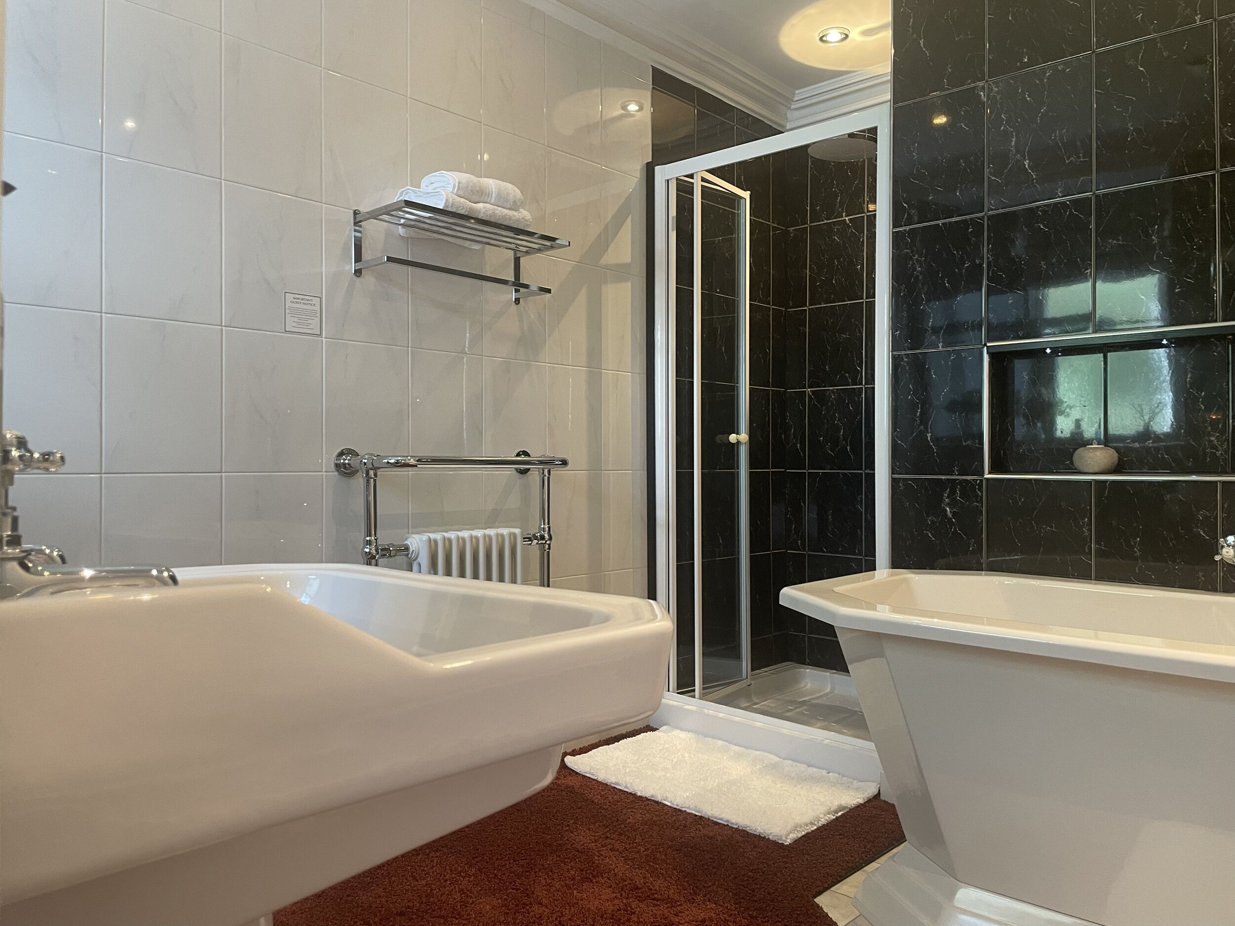 Un bagno con due vasche da bagno bianche, un box doccia in vetro e uno schienale in marmo.