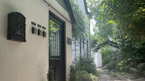 Ein Gebäude mit einer schwarzen Tür, einem Schild mit der Aufschrift 'Queensbury House' und einem kleinen Garten mit Topfpflanzen und einem Pflasterweg.