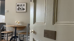 Ein Zimmer mit einem Holztisch, zwei Stühlen, einer kleinen Vase mit Blumen und einer Tür mit einem Namensschild mit der Aufschrift 'De Cressy'.