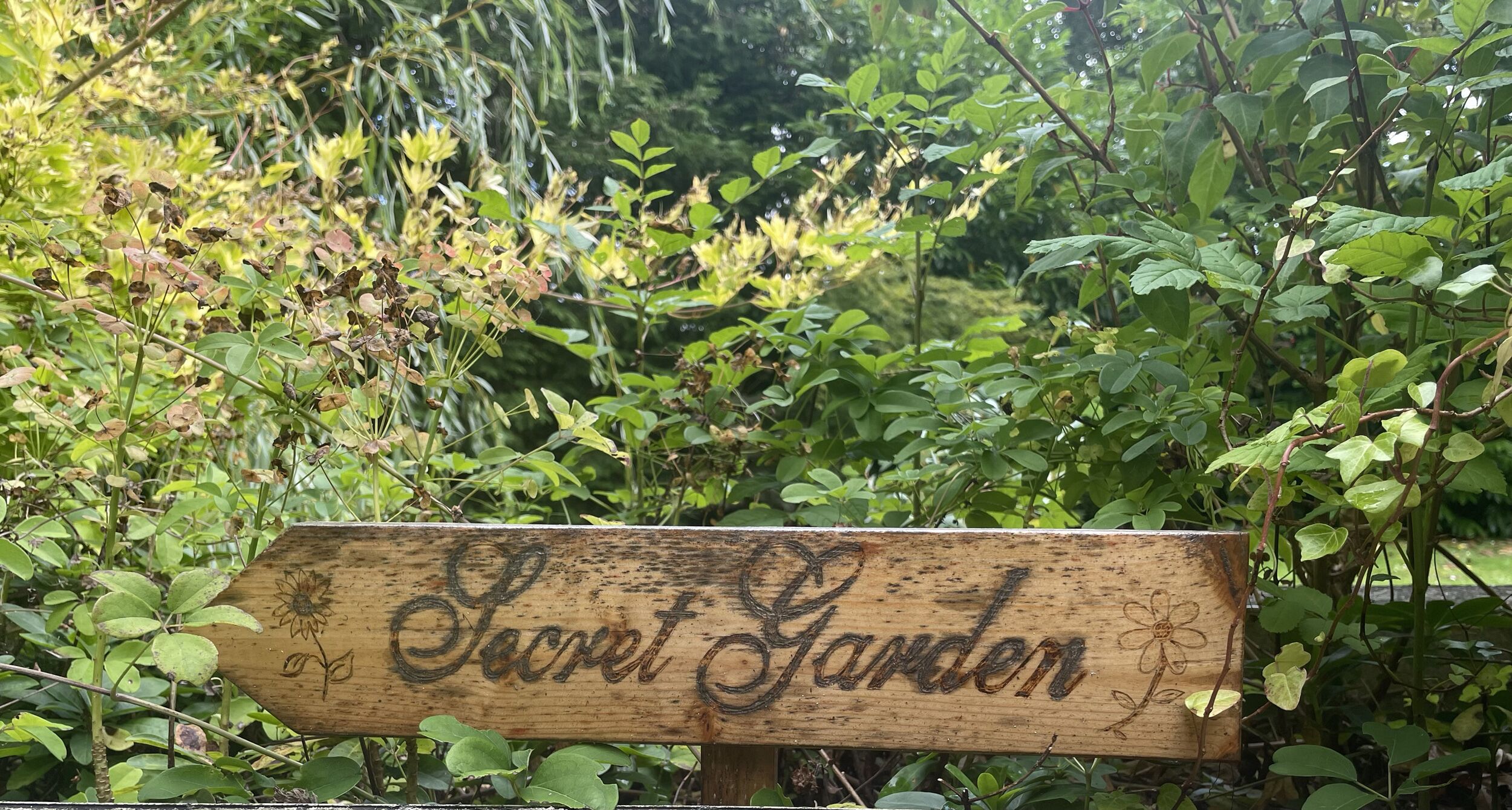 A wooden sign with the text "Secret Garden" surrounded by lush greenery.