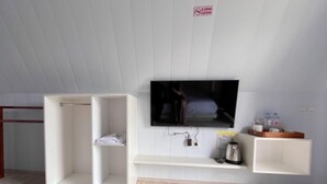 Une chambre moderne dotée d’un téléviseur à écran plat fixé au mur, d’une armoire blanche et d’une petite étagère sur laquelle se trouvent une bouilloire et d’autres objets.
