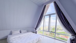 Une chambre avec une grande fenêtre, un lit et une vue sur la verdure.