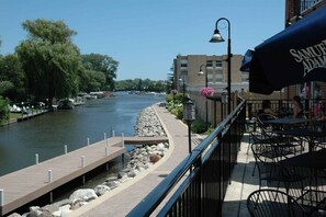 A riverside view with a wooden dock, a stone pathway, and outdoor seating with umbrellas. - McHenry Riverside Retreat – Comfort & Relaxation (McHenry)