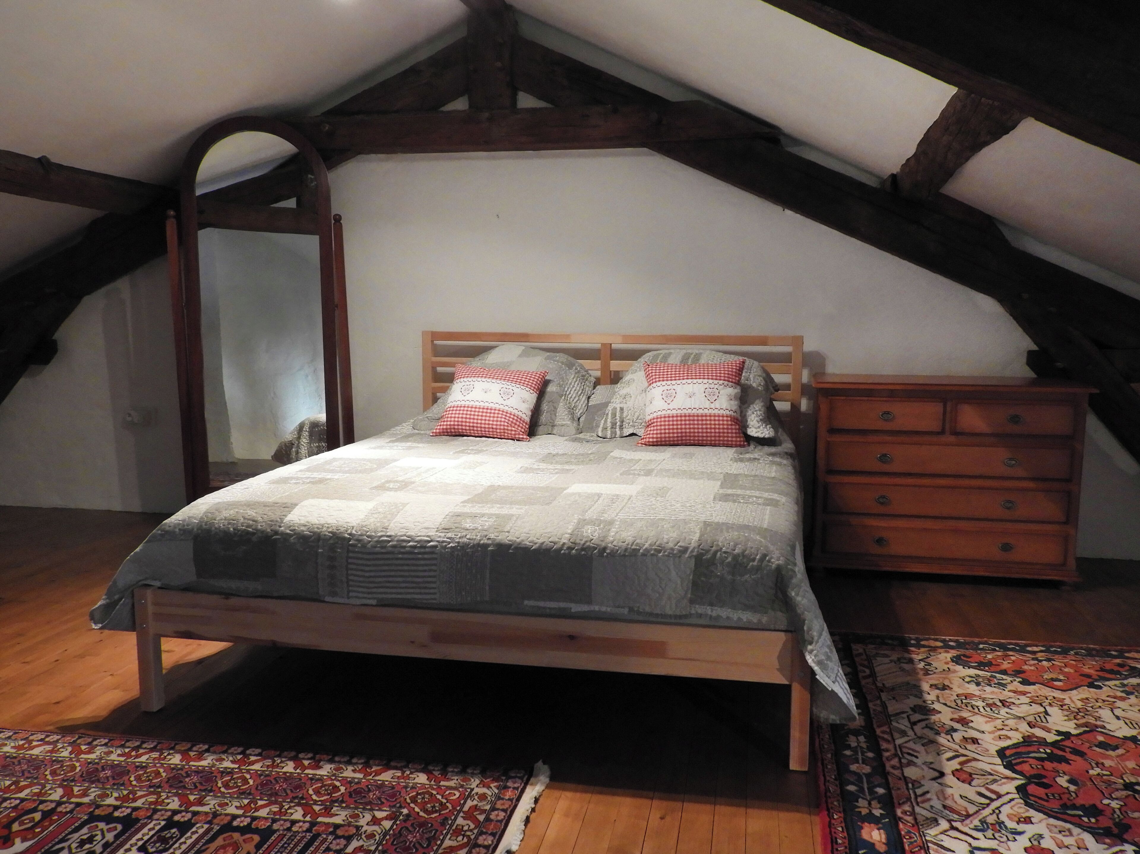 A bedroom with a wooden bed, a dresser, and a patterned rug.