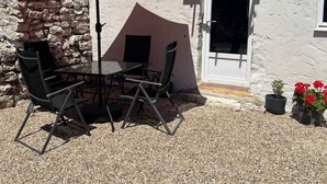 Een terras buiten met een tafel, stoelen, een rode parasol en potplanten.