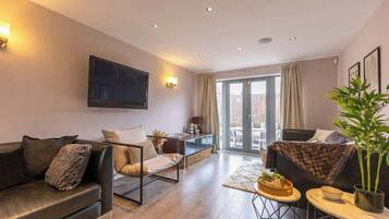 A modern living room with a sofa, armchair, and a dining area with a table and chairs.