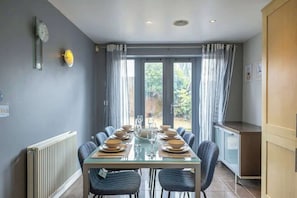 A dining area with a table set for six, a radiator, a clock, and a view of the outdoors.