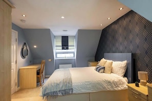 A bedroom with a bed, bedside tables, a desk, and a window.