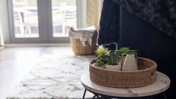 A wicker basket with plants on a small round table, a dark sofa, and a view of outdoor seating through a glass door.
