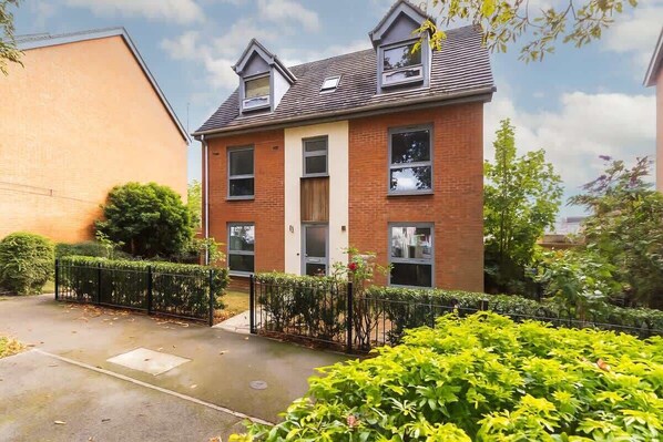 A two-story residential building with a brick facade, dormer windows, and a small garden area with a fence.