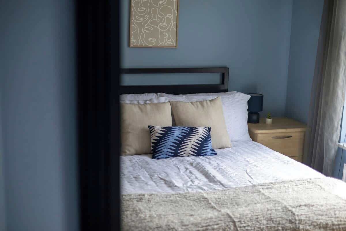 A bedroom with a bed, a nightstand, a lamp, and a wall art piece.